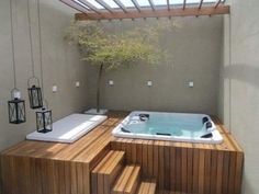 a hot tub sitting on top of a wooden table next to a tree and lanterns