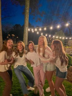 four girls are posing for the camera in front of string lights and trees at night