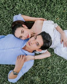 two people laying on the ground in grass looking up at the camera with their arms around each other