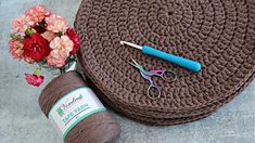 yarn, crochet hooks, and scissors are sitting on the floor next to a flower vase