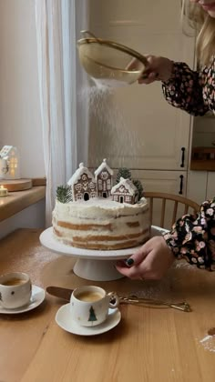 a woman is pouring frosting onto a cake on a table with cups and saucers