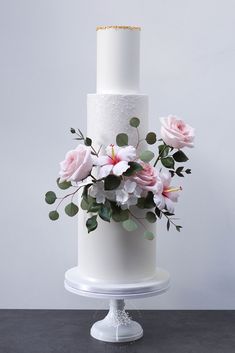 a three tiered white wedding cake with pink flowers and greenery on the top