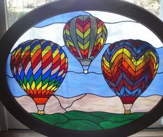 two hot air balloons are in the sky on a stained glass window frame, with mountains and blue sky behind them