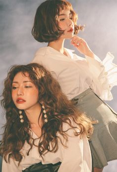 two beautiful young women standing next to each other in front of a blue sky with clouds