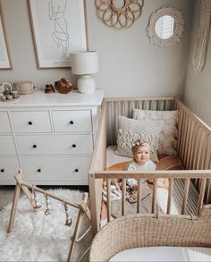 a baby sitting in a crib next to a dresser and bed with white rugs