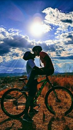 a man and woman kissing while sitting on top of a bike in front of the sun