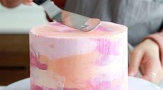 a person using a knife to cut a cake with pink and orange paint on it