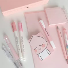 some pens and notebooks are laying on a pink surface with an eraser next to it