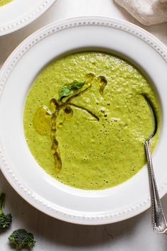 two white bowls filled with green soup on top of a table