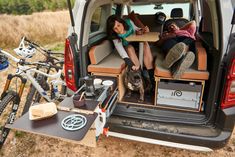 two women sitting in the back of a van with their dogs and bicycles behind them