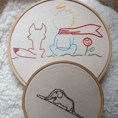 two embroidery hoops with designs on them sitting on a white blanket next to each other