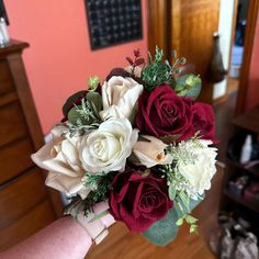 a bridal bouquet in someone's hand on a wooden floor near a dresser