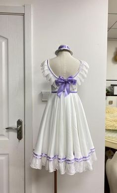 a white dress with purple trims and a bow on the front is sitting on a mannequin