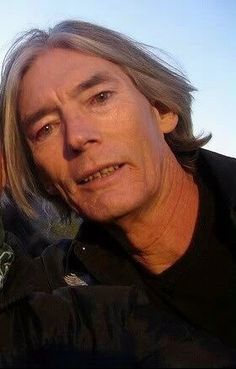 an older man with grey hair and black shirt posing for the camera while holding his hand up to his face