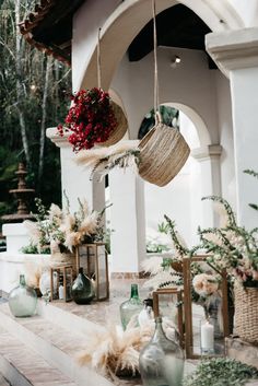 some vases with flowers hanging from them on the side of a building next to plants and candles