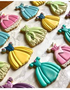 there are many decorated cookies on the table with different colors and shapes, including princess dresses