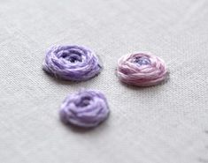 three crocheted flowers sitting on top of a white cloth