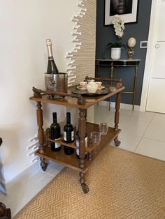 a wooden cart with wine bottles and glasses on it in a living room next to a painting