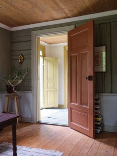 an open door leading into a room with wooden floors and walls, in front of a bench