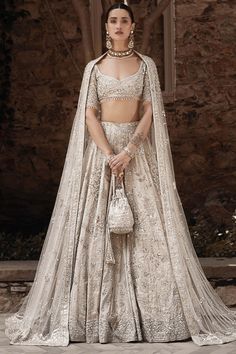 a woman in a white lehenga with an intricate cape on her head and handbag