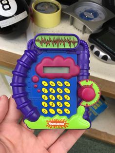 a hand holding a toy cell phone in front of a table with other items on it