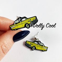 a pair of yellow and black car earrings on a woman's hand with the words dolly cool written above it