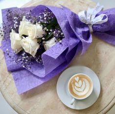 a bouquet of white roses sitting on top of a table next to a cup of coffee