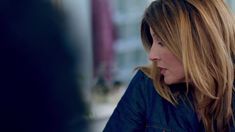 a woman with long hair is talking to someone in front of a window and looking off into the distance