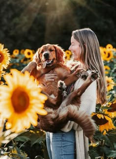 a woman holding a brown dog in her arms and smiling at the camera with sunflowers behind her