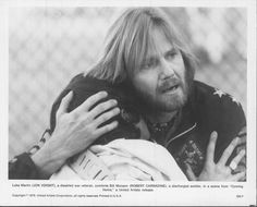 a black and white photo of a man with long hair hugging another man's shoulder