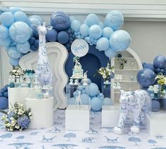 a blue and white baby shower party with balloons on the wall, cake table and elephant figurines