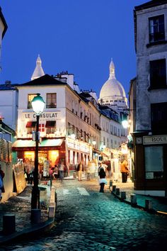 people are walking down the cobblestone street in an old european city at night