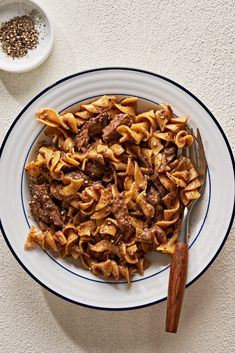 a white plate topped with pasta covered in meat and sauce next to a bowl of seasoning