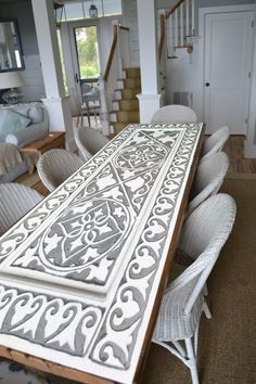 a dining room table with white chairs and an intricate design on the top, in front of a staircase