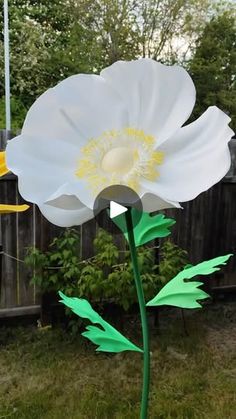 a large white flower sitting on top of a lush green grass covered field next to a wooden fence