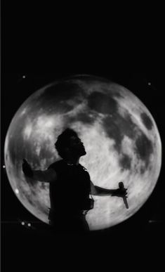 a person standing in front of a full moon with their arms spread out to the side