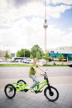 a woman riding a green bike down a street next to a tall tower with a sky scraper in the background