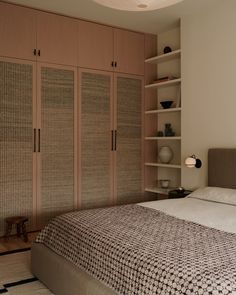 a large bed in a bedroom next to wooden closets and bookshelves on the wall