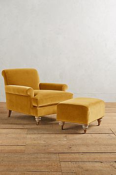 a yellow chair and footstool sitting on top of a hard wood floor next to a white wall