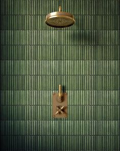 a green tiled wall with a brass shower head and hand held shower faucet