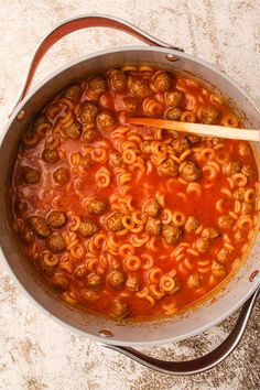 a pot filled with pasta and meatballs on top of a table next to a wooden spoon