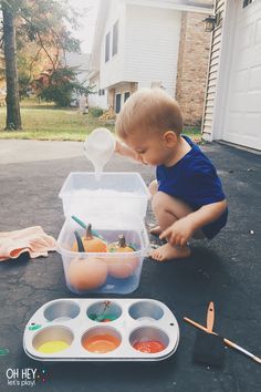 a toddler playing with an egg carton filled with paint and eggs in front of a house