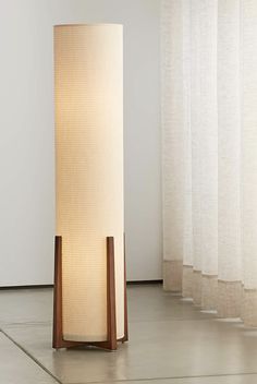 a floor lamp sitting on top of a wooden stand next to a curtained window