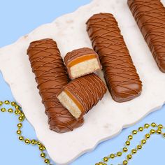 three pieces of chocolate covered candy on a white plate with gold beaded necklaces