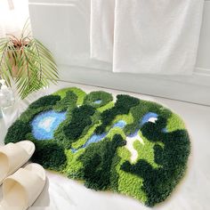 a green rug with blue and white designs on the floor next to towels, slippers and plant