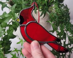 a hand holding a stained glass cardinal ornament in front of a potted plant