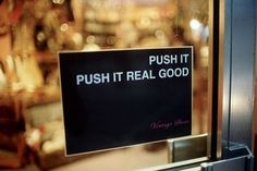 black and white photograph of a push it real good sign in a store front window