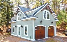 a gray and white house in the woods with two garages on each side, surrounded by pine trees