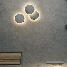 three circular lights are mounted on the wall above a table and bench in front of a concrete wall