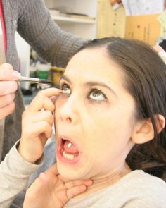 a woman getting her make - up done while another person is holding scissors in front of her